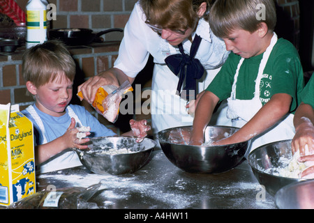 Les jeunes garçons le pétrissage la pâte dans un bol et faire un gâchis de la farine dans la cuisine tout en apprenant à cuire Banque D'Images