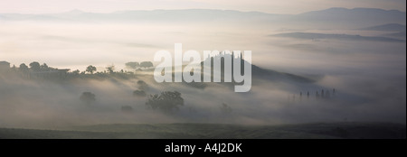 Ferme entourée de cyprès sur une colline parmi des brouillards matinaux, Val D'Orcia, Toscane, Italie Banque D'Images