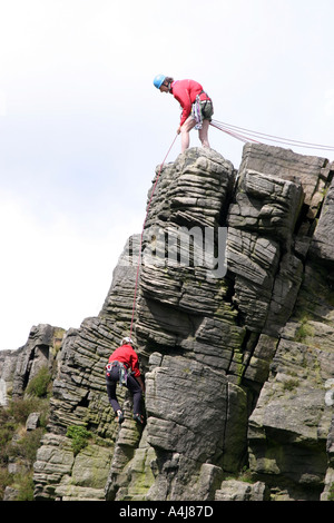 Alpinistes sur Windgather rochers sur le côté est du Peak District, Derbyshire, Angleterre. L'homme au haut des rochers est l'assurage d'un grimpeur sur le chemin vers le haut. Banque D'Images