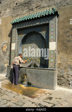 Obtenir de l'eau l'homme à partir de la fontaine murale est soignée dans les mosaïques, Meknès, Moyen Atlas, Maroc Banque D'Images