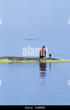 Homme aux deux meilleurs amis, le chien et cellulaire, sur petite île rocheuse à l'archipel de Stockholm Banque D'Images