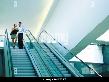 Couple riding down escalator, smiling Banque D'Images