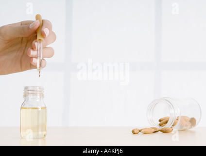 Woman's hand holding compte-gouttes d'huile essentielle d'amandes et de répandre de jar Banque D'Images