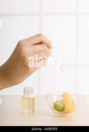 La main de femme laissant tomber l'huile dans un bol avec le zeste de citron Banque D'Images