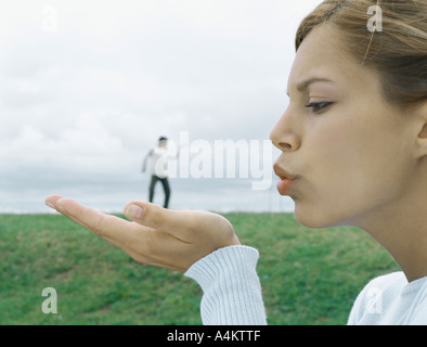 Femme en premier plan de palm et soufflant kiss, l'homme en arrière-plan lointain, illusion optique Banque D'Images