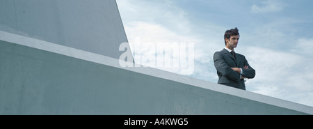 Homme debout derrière mur de béton avec bras croisés, low angle view Banque D'Images