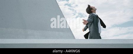 Homme debout derrière mur de béton avec les bras tendus, side view Banque D'Images