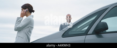 La femme et l'homme en costume, debout près de voiture, man looking at camera, Woman talking on cell phone Banque D'Images