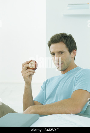 Young man sitting at table holding up apple en main Banque D'Images