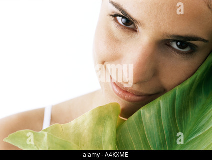 Femme tilting head contre green leaf, smiling, portrait Banque D'Images