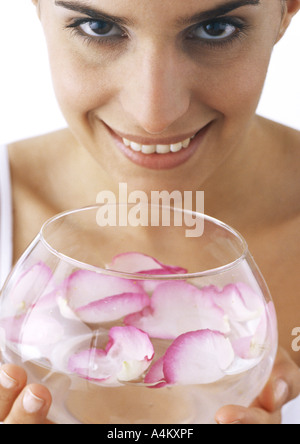 Woman holding bowl de pétales de rose flottant dans l'eau, looking at camera, close-up Banque D'Images