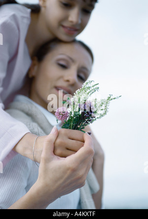 Girl embracing mère par derrière, la main de la mère de la jeune fille au bouquet de fleurs sauvages, Banque D'Images