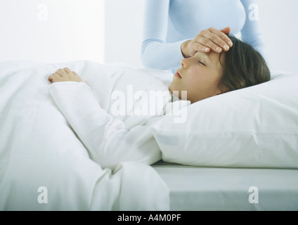 Fille au lit sous les couvertures, woman's hand sur le front de la jeune fille Banque D'Images