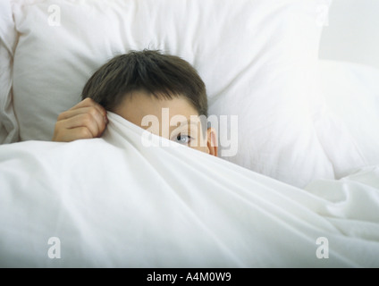 Boy in bed, peeking out derrière feuille avec un oeil Banque D'Images