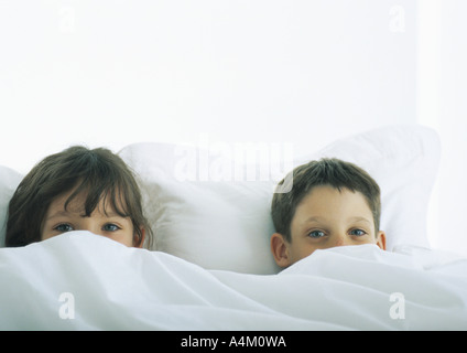 Garçon et fille au lit, visages partiellement couvert par couette Banque D'Images