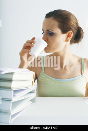 Femme à boire à table avec pile de dossiers Banque D'Images