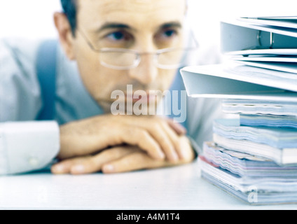 Man resting head on hands, à la pile de dossiers à Banque D'Images