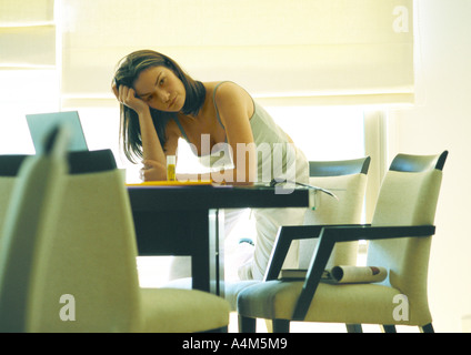 Jeune femme travaillant à la maison, se penchant sur la table Banque D'Images