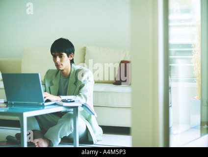 Jeune homme assis sur le plancher, en utilisant un ordinateur portable sur une table basse Banque D'Images