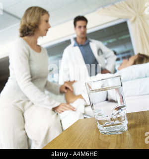 Verre d'eau sur la table et patient recevant une visite du médecin homme et femme Banque D'Images