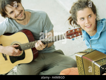 Jeune homme jouant de la guitare, jeune femme jouant de l'accordéon Banque D'Images