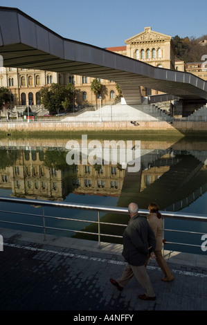 Deux personnes marchant vers Puente Pedro Arrupe, pont de l'Université Deusto de refléter dans l'arrière-plan, la rivière Nervion Bilbao Banque D'Images