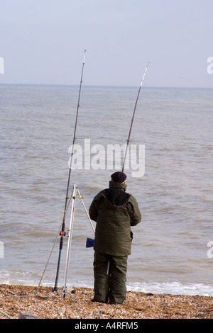 Un beachcasting pêcheur regardant la mer ses lignes sur la plage de galets à Dungeness. Banque D'Images