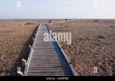 Les touristes prendre la promenade vers la mer de l'autre côté de la plage de galets à Dungeness, dans le Kent Banque D'Images