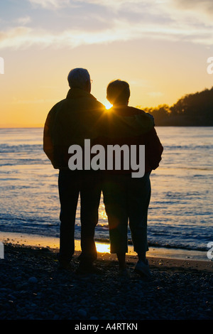 Silhouette de couple regardant le coucher du soleil sur la plage Banque D'Images