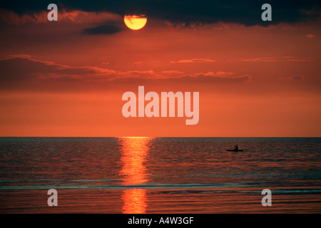 Robert un requin appelant de Kontu paddles jusqu'à la limite du récif au coucher du soleil pour faire des incantations de lui apporter chance dans sa hun Banque D'Images