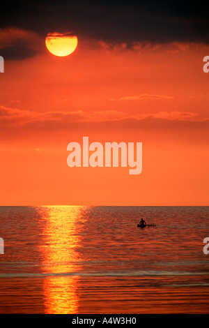 Robert un requin appelant de Kontu paddles jusqu'à la limite du récif au coucher du soleil pour faire des incantations de lui apporter chance dans sa hun Banque D'Images