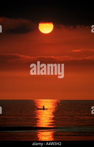 Robert un requin appelant de Kontu paddles jusqu'à la limite du récif au coucher du soleil pour faire des incantations de lui apporter chance dans sa hun Banque D'Images