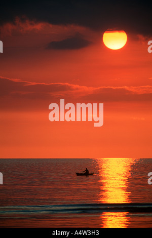 Robert un requin appelant de Kontu paddles jusqu'à la limite du récif au coucher du soleil pour faire des incantations de lui apporter chance dans sa hun Banque D'Images