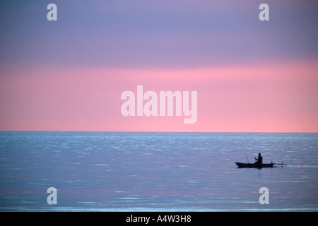 Robert un requin appelant de Kontu paddles jusqu'à la limite du récif au coucher du soleil pour faire des incantations de lui apporter chance dans sa hun Banque D'Images