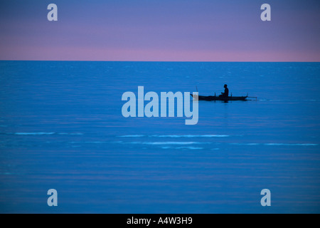 Robert un requin appelant de Kontu paddles jusqu'à la limite du récif au coucher du soleil pour faire des incantations de lui apporter chance Banque D'Images