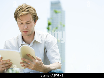 Young man reading book, gratte-ciel en arrière-plan Banque D'Images