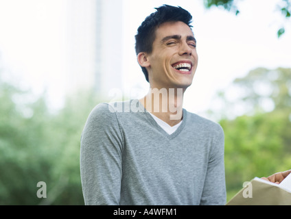 Jeune homme livre de lecture et de rire dans le parc urbain Banque D'Images