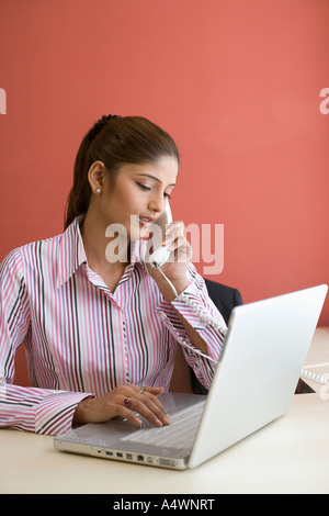 Businesswoman talking on phone while using laptop Banque D'Images