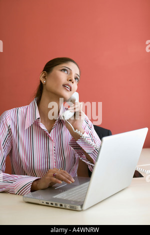 Businesswoman talking on phone while using laptop Banque D'Images