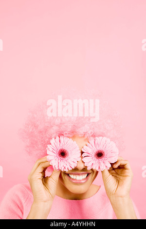 Femme portant une perruque rose et holding Flowers over eyes Banque D'Images