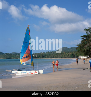 Double coque catamaran Hobie Cat at waters edge de Choc Beach couple en train de marcher côte ouest des Caraïbes Sainte-Lucie Banque D'Images