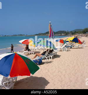 Les gens sous le soleil soleil brollies colorés sur la plage de Reduit avec Rodney Bay au-delà de la côte nord-ouest des Caraïbes Sainte-Lucie Banque D'Images