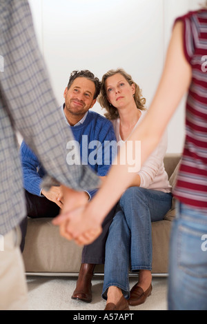 Teenage couple holding hands, parents sitting on sofa Banque D'Images