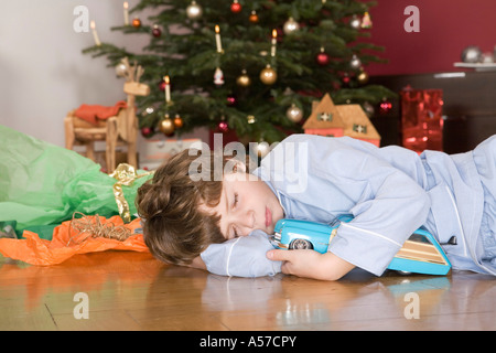 Boy (4-7) sleeping under Christmas Tree, holding toy car Banque D'Images