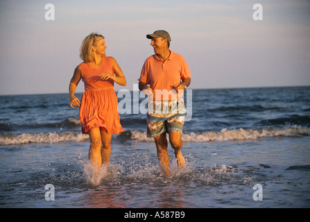 Couple marié adultes fonctionnant en eau peu profonde sur la plage Banque D'Images