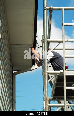 Menuisier travaillant à partir d'une tour d'accès en aluminium en installant un nouveau UPVC en plastique Sur-revêtement à l'eaves existant soffit board fascia Angleterre Royaume-Uni Banque D'Images