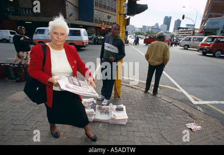 Une femme âgée en passant devant un vendeur de journaux dans les rues de Johannesburg Afrique du Sud Banque D'Images