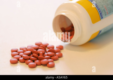 Comprimés comprimés rouge vif renverse un flacon de médicaments génériques sur un fond blanc Banque D'Images
