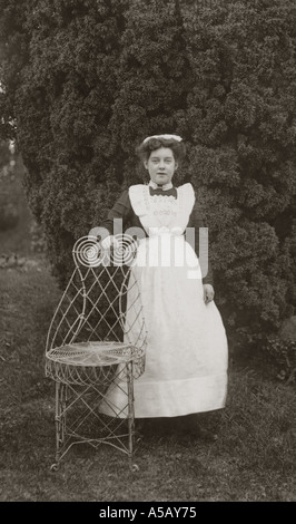 Portraits professionnels originaux carte postale d'Edwardian housemaid posant dans le jardin d'une maison de campagne à côté de la chaise, Cumbria, vers 1905, Royaume-Uni Banque D'Images