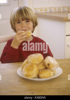 Jeune garçon de s'asseoir à une table de cuisine manger une assiette de beignets Banque D'Images